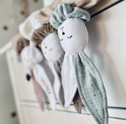 Ročno izdelane nanice za novorojenčka v pastelnih barvah, obešene na otroški posteljici